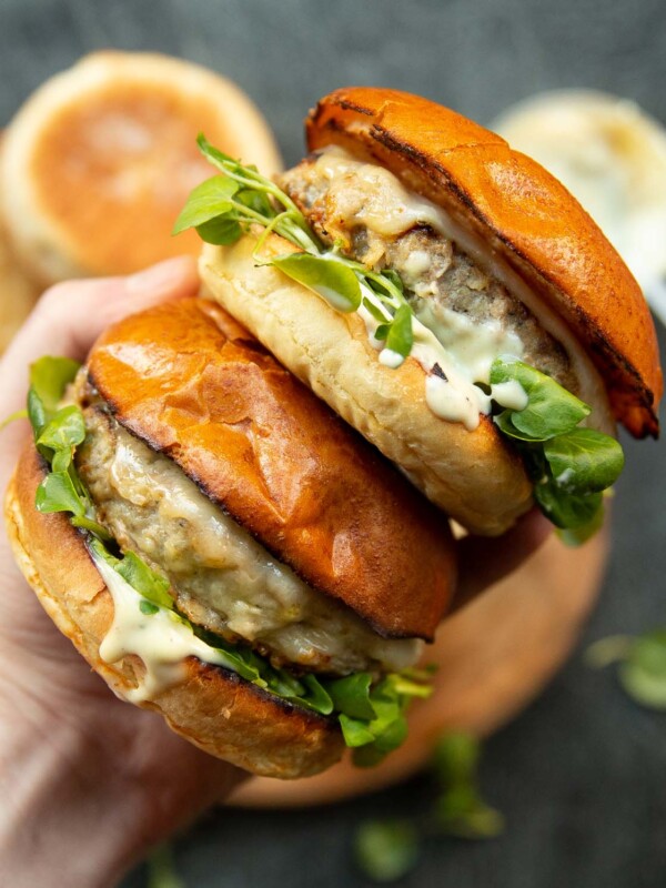 overhead shot of hand holding two burgers above ingredients