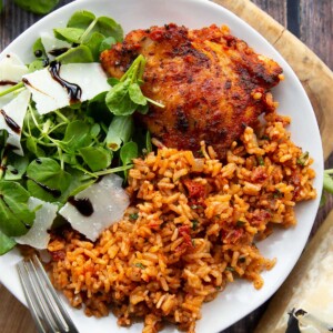 overhead shot of chicken served with rice on small white plate with salad