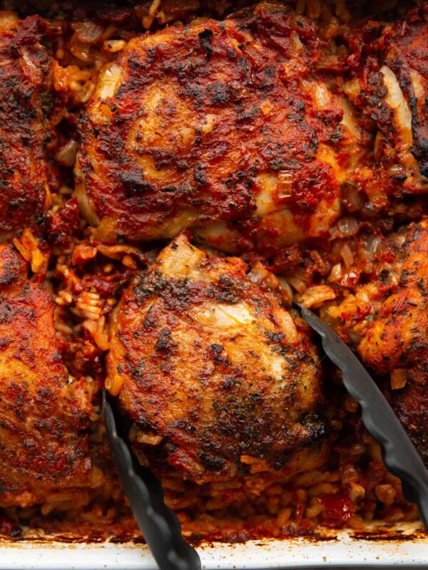 overhead shot of chicken and rice freshout the oven with tongs grabbing chicken