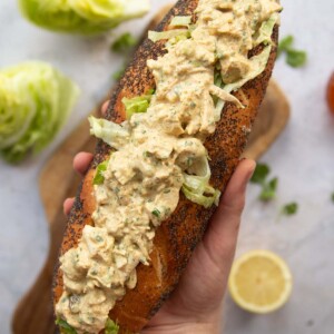 overhead shot of hand holding baguette filled with coronation chicken above garnish