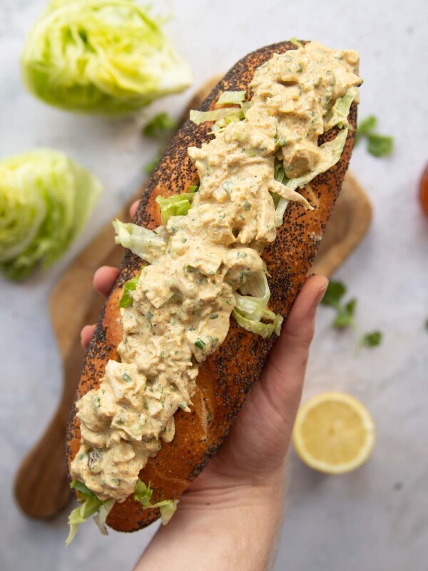 overhead shot of hand holding baguette filled with coronation chicken above garnish