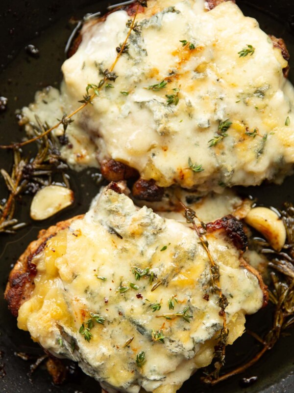 overhead shot of pork chops with applesauce and melted blue cheese in pan