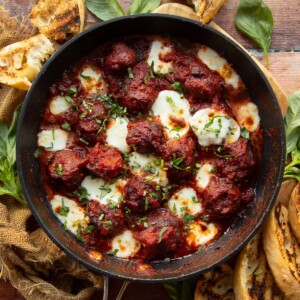 overhead shot of meatballs in skillet surrounded by fresh basil and garlic bread