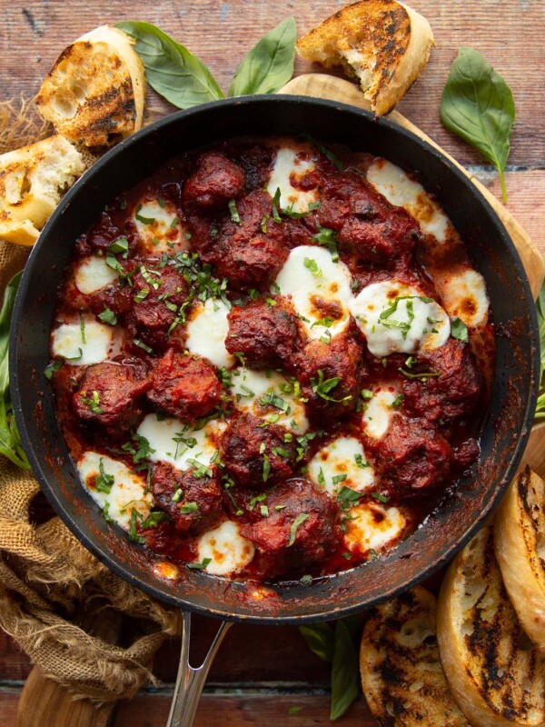 overhead shot of meatballs in skillet surrounded by fresh basil and garlic bread