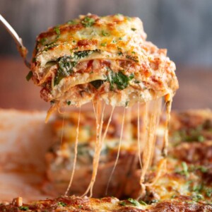 lifting lasagne from baking dish with cheese pouring down