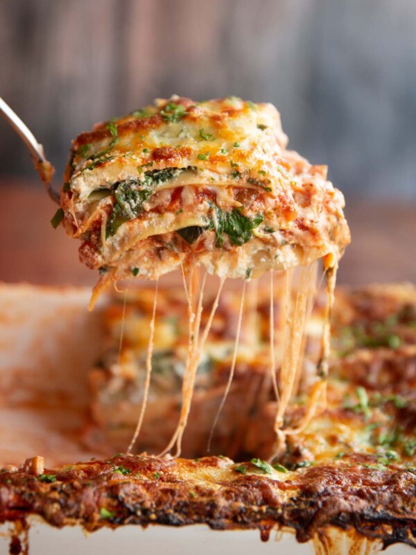 lifting lasagne from baking dish with cheese pouring down