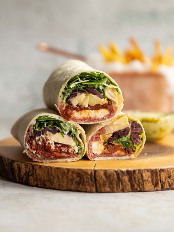 3 wraps stacked on each other on wooden board with dip and fries blurred in background