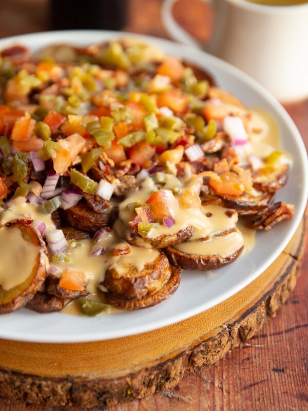 potato nachos on large white plate with can of Guinness and pot of cheese sauce blurred in background