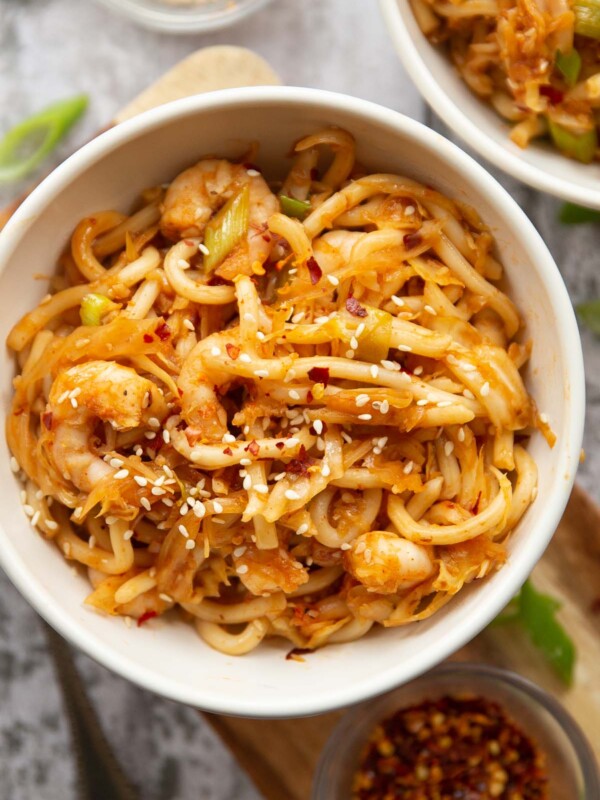 overhead shot of noodles in small white bowl garnished with chilli flakes and sesame seeds