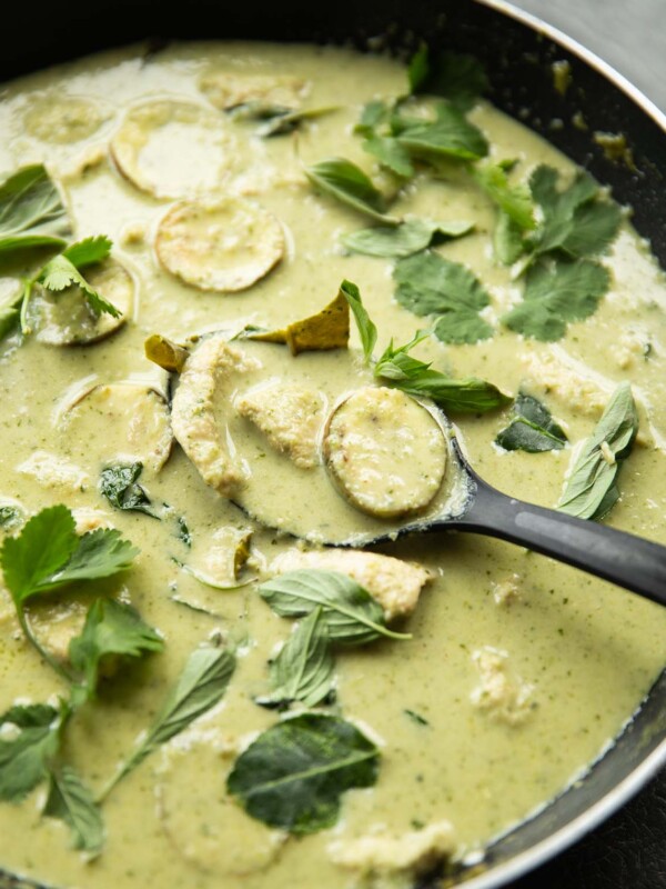 black serving spoon digging in to large pan of green curry