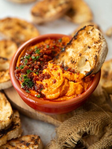 dip served in small red bowl with ciabatta dunked in