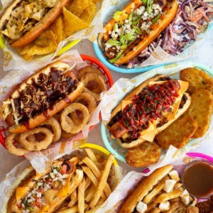 overhead shot of 6 hot dogs in coloured baskets with range of sides