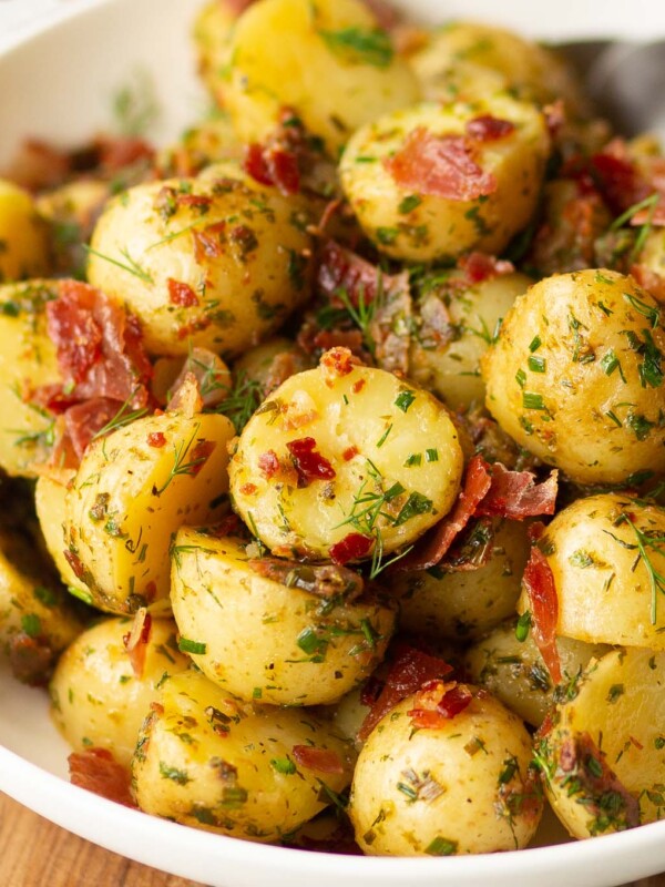 herbed potato salad served in white bowl with 2 silver spoon blurred in background