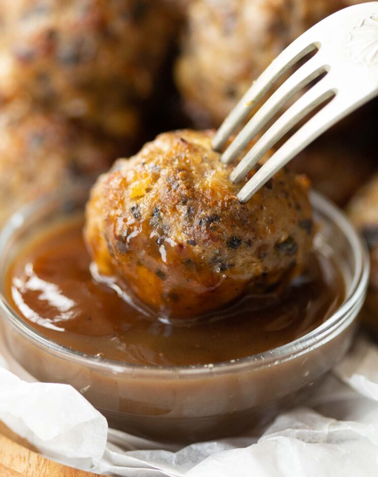 silver fork dunking breakfats meatball into small glass pot of brown sauce