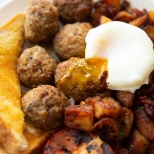 breakfast meatballs on white plate served with poached egg, toast tomato and potatoes