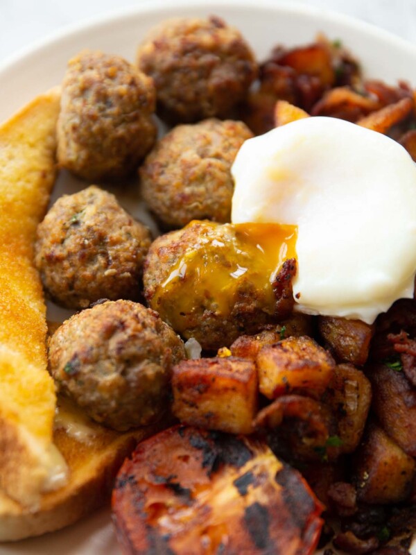 breakfast meatballs on white plate served with poached egg, toast tomato and potatoes