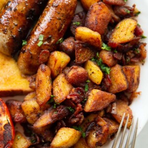 overhead shot of breakfast potatoes on white plate served with sausages, tomato and toast