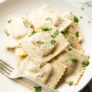 ravioli served on white plate garnished with parsley with silver fork