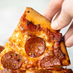 close up shot of hand lifting up slice of pepperoni pizza