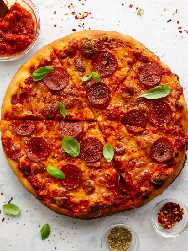 overhead shot of pizza sliced up on white background surrounded by chilli flakes and oregano