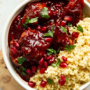 overhead shot of pomegranate chicken in small white bowl served with couscous