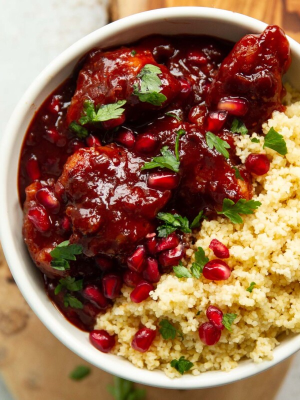 overhead shot of pomegranate chicken in small white bowl served with couscous