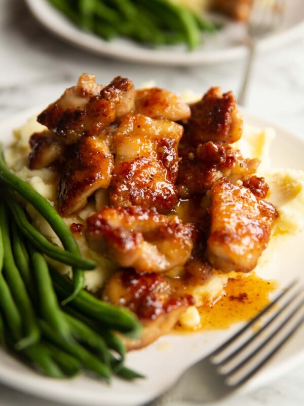 honey butter chicken on bed of mashed potato with green beans on small white plate