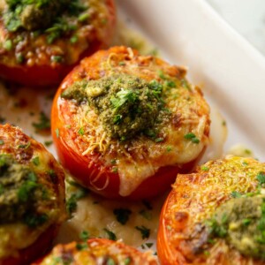 stuffed tomatoes in large white baking dish fresh out the oven with dollop of pesto