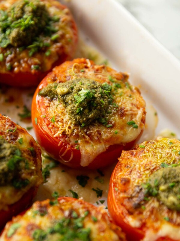 stuffed tomatoes in large white baking dish fresh out the oven with dollop of pesto