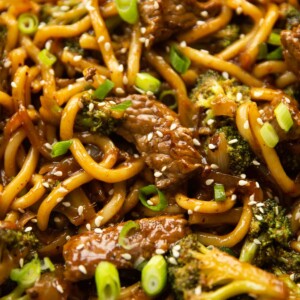 close up shot of beef and broccoli noodles in skillet garnished with sesame seeds and spring onion