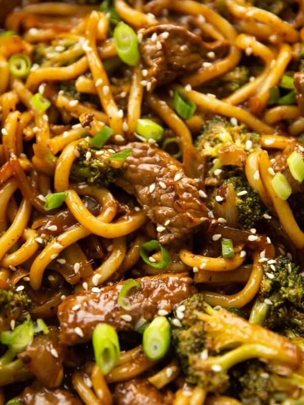 close up shot of beef and broccoli noodles in skillet garnished with sesame seeds and spring onion