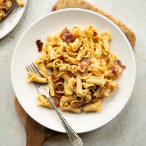 overhead shot of brie pasta on white plate with silver fork on wooden chopping board