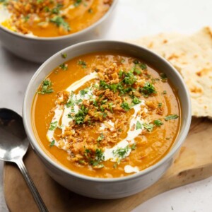 curried sweet potato soup served in large grey bowl on wooden board with silver spoon and flatbread