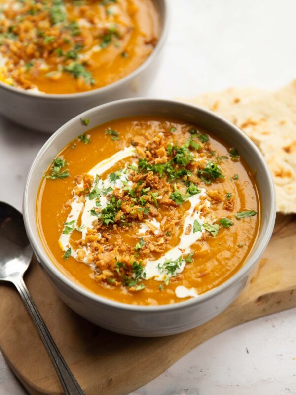 curried sweet potato soup served in large grey bowl on wooden board with silver spoon and flatbread