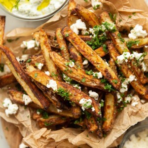 close up overhead shot of Greek fries in brown paper garnished with feta and parsley