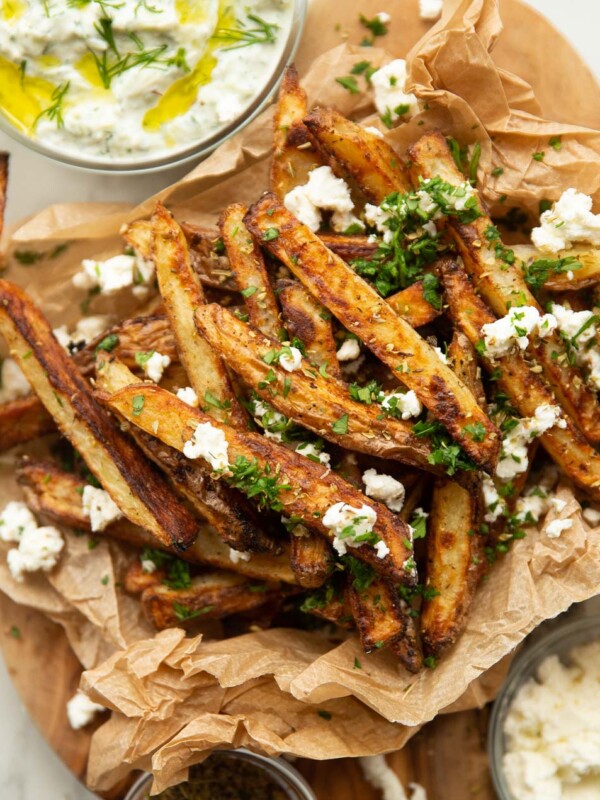 close up overhead shot of Greek fries in brown paper garnished with feta and parsley