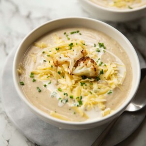 cauliflower soup served in small white bowl on marble background garnished with cheese and chives