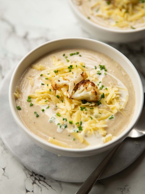 cauliflower soup served in small white bowl on marble background garnished with cheese and chives