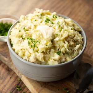 mashed potatoes in large grey bowl on wooden chooping board garnished with chives