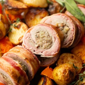 close up shot of sliced stuffed pork tenderloin on bed of roasted veg