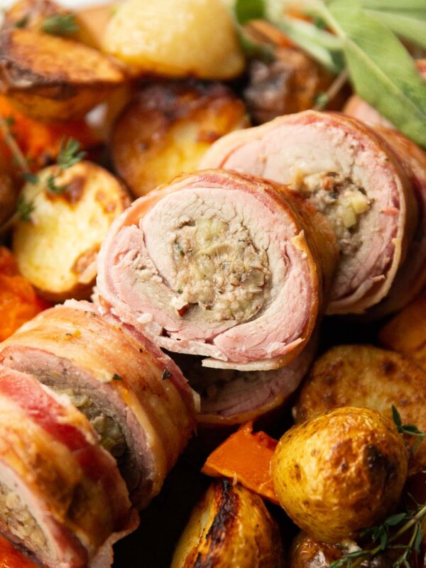 close up shot of sliced stuffed pork tenderloin on bed of roasted veg