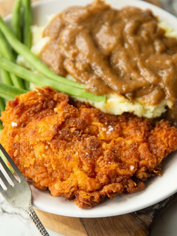 fried chicken cutlet served on small white plate with green beans, mash and gravy