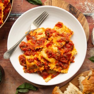 overhead shot of ravioli served on small white plate on wooden board with silver fork