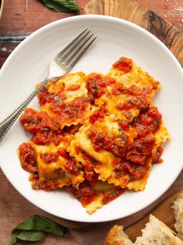 overhead shot of ravioli served on small white plate on wooden board with silver fork