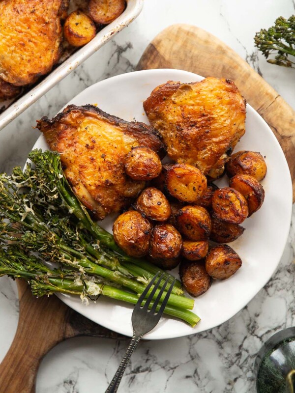 overhead shot of baked chicken and potatoes served on small white plate with tenderstem broccoli