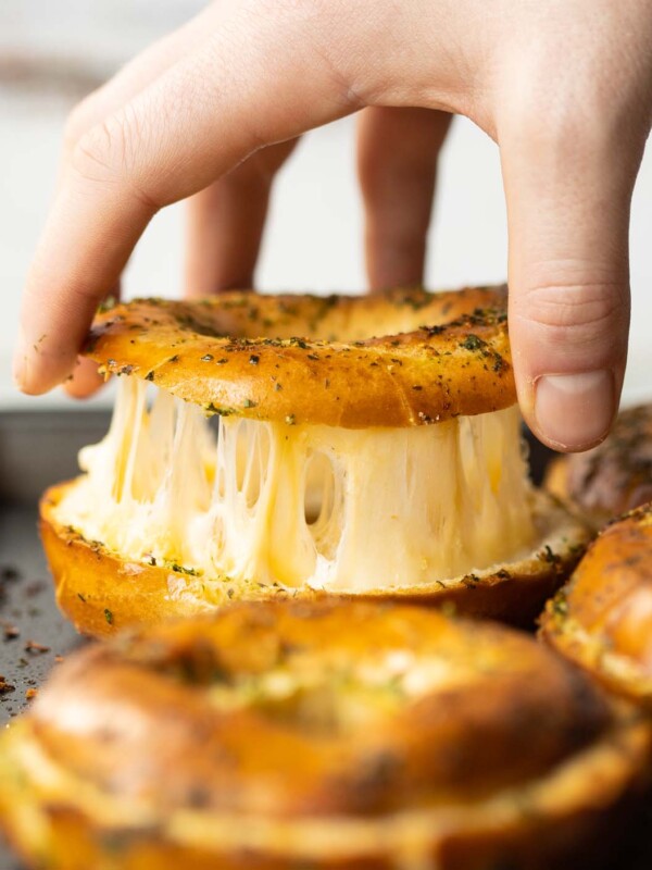 close up shot of hand lifting lid of bagel with cheese pull