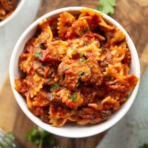 overhead shot of mushroom tomato pasta in small white bowl on wooden chopping board