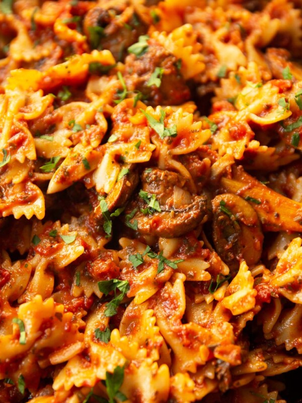 close up shot of tomato and mushroom pasta in skillet with wooden spoon digging in