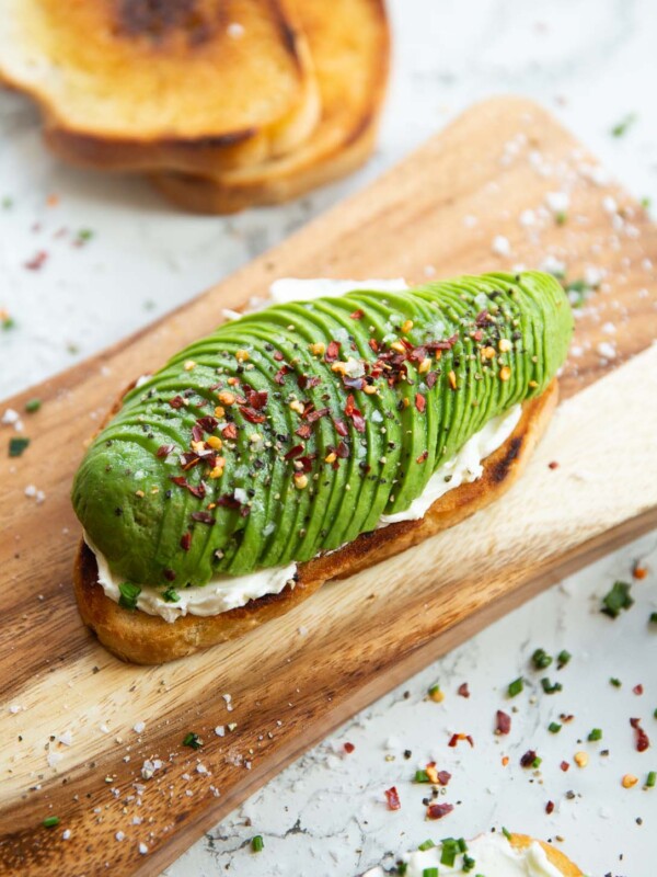 close up shot of avocado cream cheese toast on chopping board surrounded by garnish