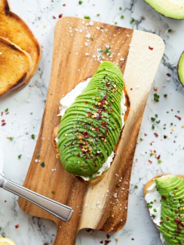 overhead shot of cream cheese avocado toast on chopping board surrounded by garnish